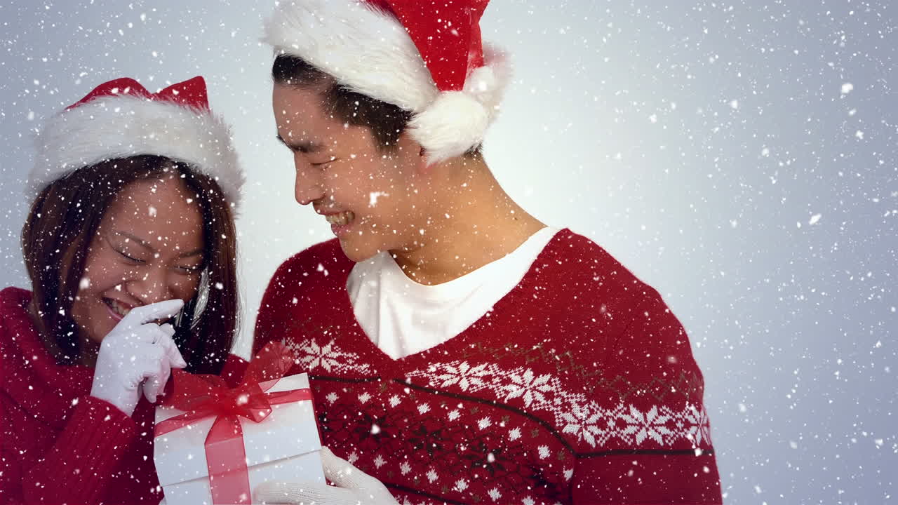 composición de video con nieve cayendo sobre pareja feliz con regalo