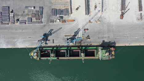 a cargo ship being loaded at a busy port during daylight, aerial view