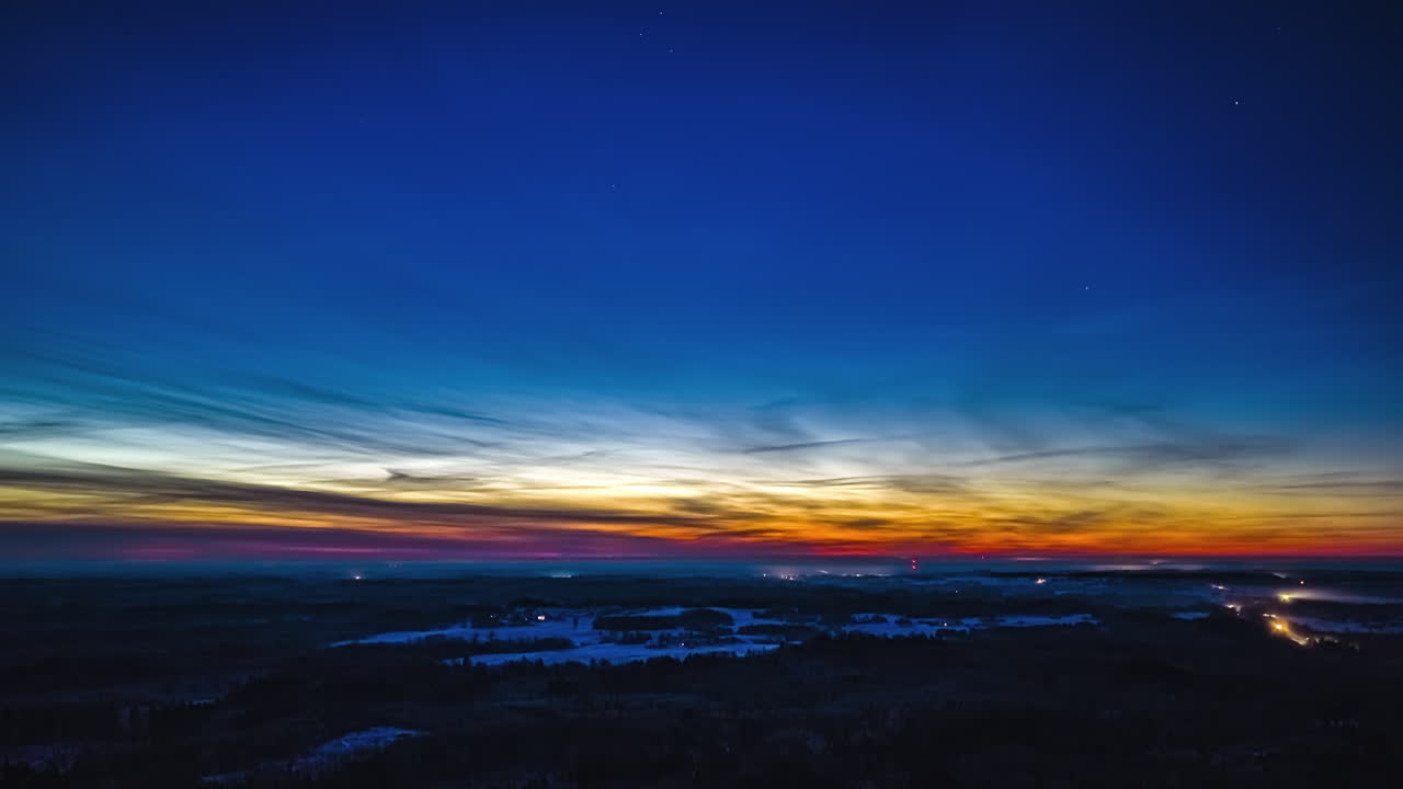 Cielo mattutino con alba in hyperlapse aereo sopra un paesaggio invernale, fari di auto in timelapse che si muovono lungo la strada con ampio cielo blu sopra.
