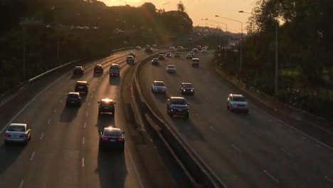 sunset glows on the tarmac of an auckland motorway as traffic rushes by