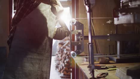 Midsection-of-caucasian-male-knife-maker-in-workshop-using-sander