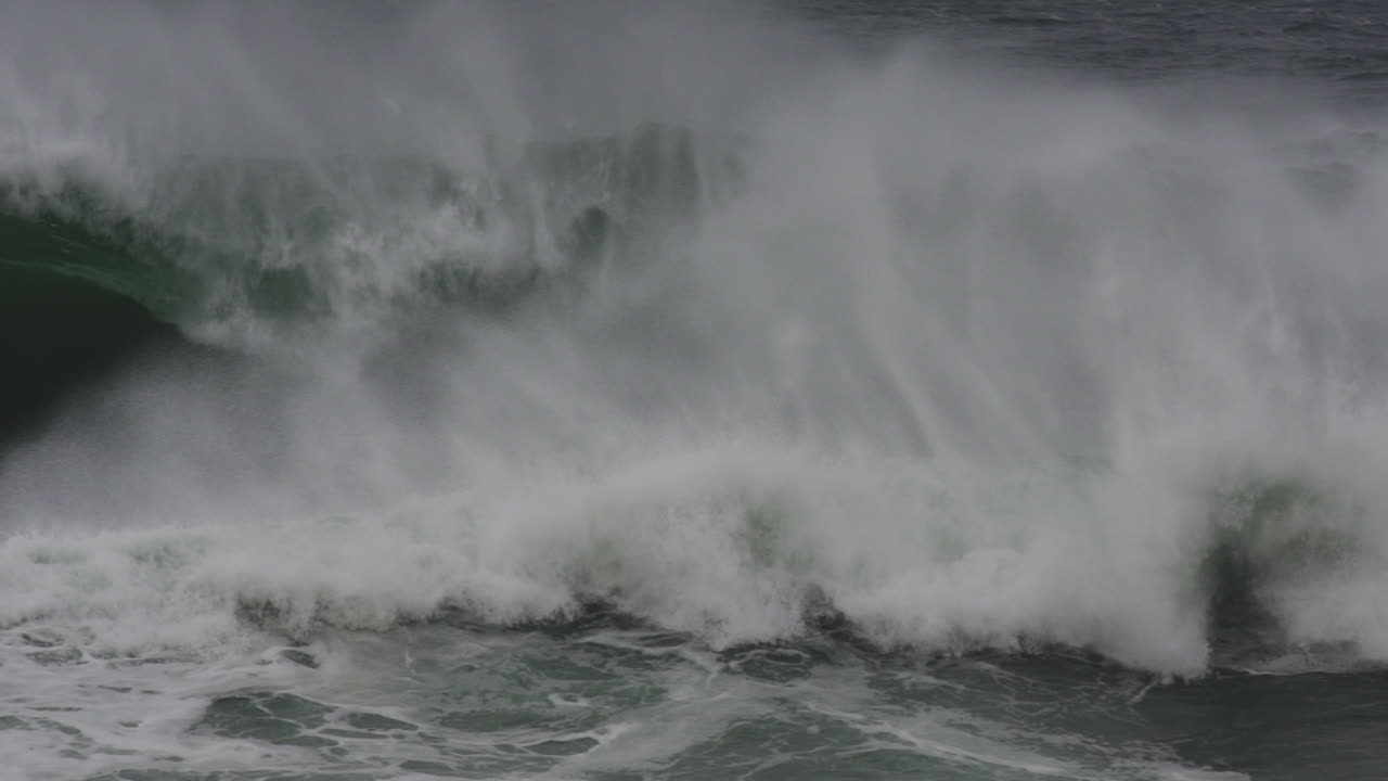 Ocean wave barrels with force and mist explosion under moody sky in slow motion