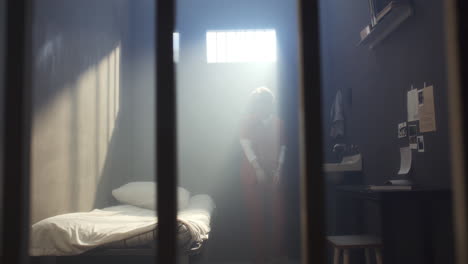 female inmate in handcuffs and uniform wandering around prison cell