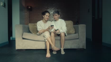 two women relaxing on a sofa with mobile phones