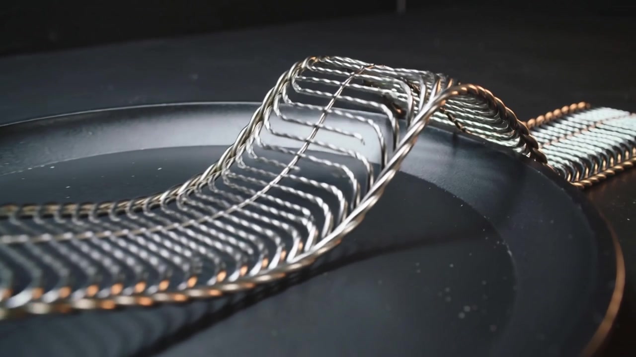 Lifting woven metal braid waving over black plate as playback starting, revealing braided handle