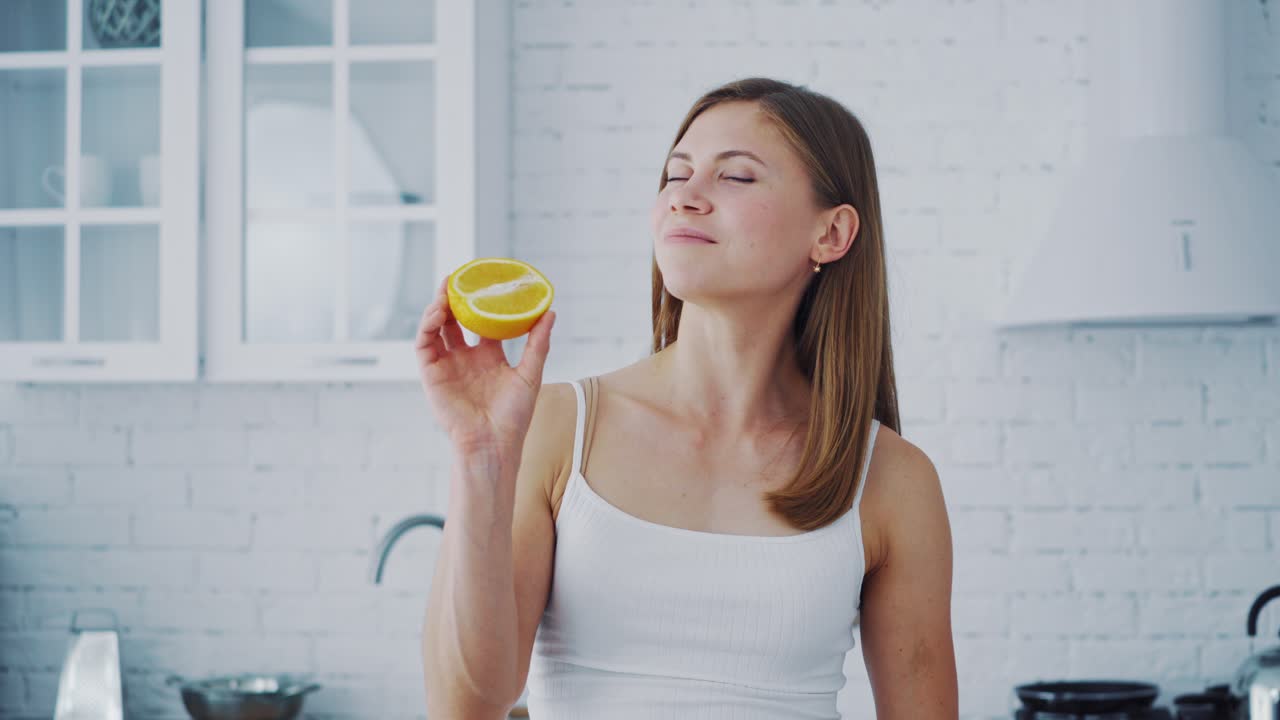 Young woman with orange in cosy kitchen. Healthy fruit in woman's hands indoors. Beautiful female holding half of juicy orange. Dieting concept.