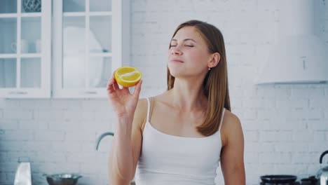young woman with orange in cosy kitchen. healthy fruit in woman's hands indoors. beautiful female holding half of juicy orange. dieting concept.