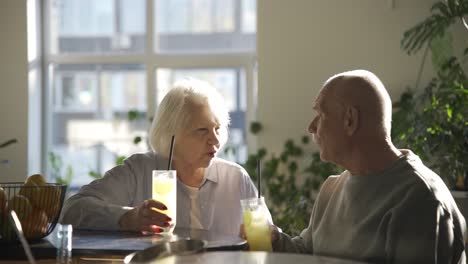 senior couple drinking limonade and talking while they are sitting in a bar at sunset