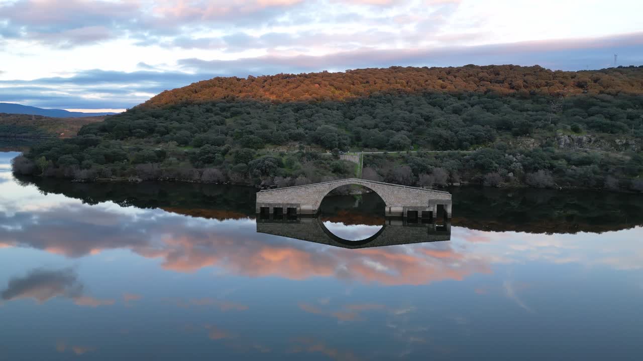 Guijo de Granadilla, Extremadura'da gün batımında El Ponton Roma Köprüsü'nün havadan drone görünümü. Tarihi taş yapının üzerinde sıcak altın rengi ışık.