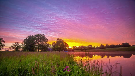 Tiro-De-Hiperlapso-Del-Cielo-Colorido-Del-Amanecer-Sobre-El-Paisaje-Rural-Con-Lago-Y-Cabaña-En-El-Fondo-Al-Amanecer