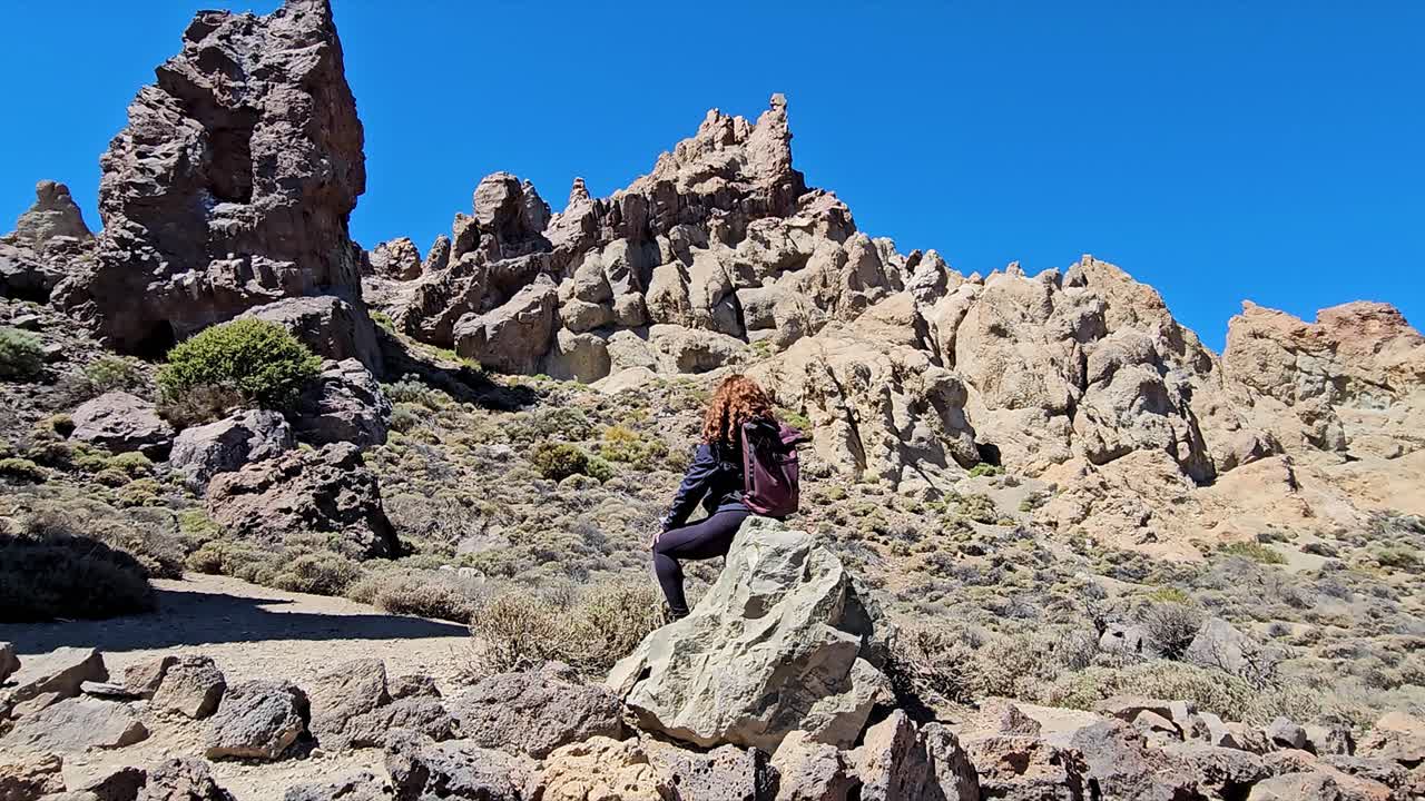 A hiker sitting on a rock at Roques de Garcia in Spain, with a clear sky