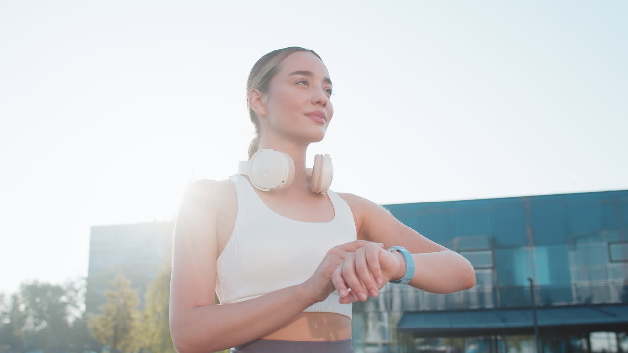 Young female runner looks at smartwatch device fitness bracelet heart rate pulse spo2 in city park
