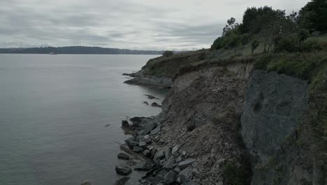 Coastline-of-rock-and-gravel-slopes-above-still-tranquil-ocean-water,-aerial