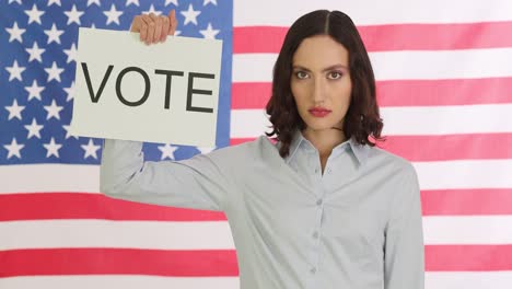 woman holding 'vote' sign in front of american flag