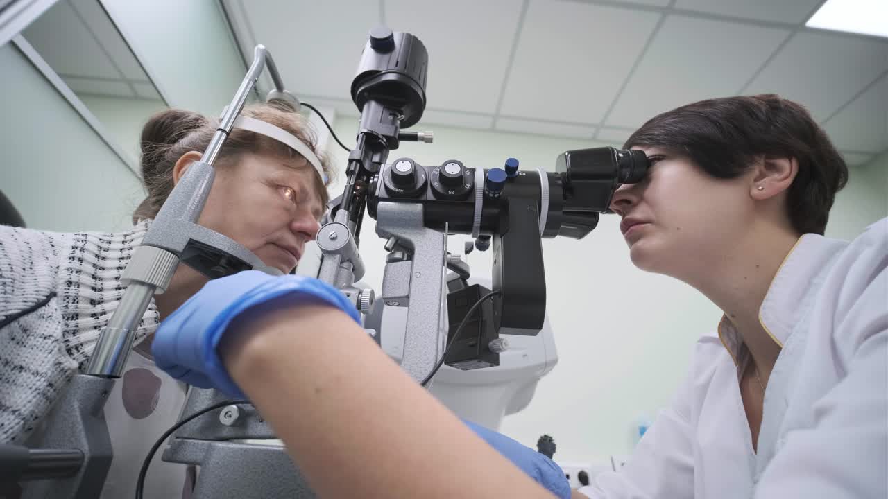 여성 의사는 안과 클리닉에서 환자의 눈을 안경으로 보고 있습니다. 시력의 전문적인 검사