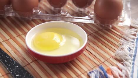 broken egg in a bowl with eggs in carton