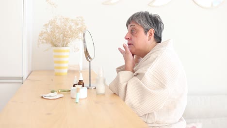 elderly woman in bathrobe applying facial cream