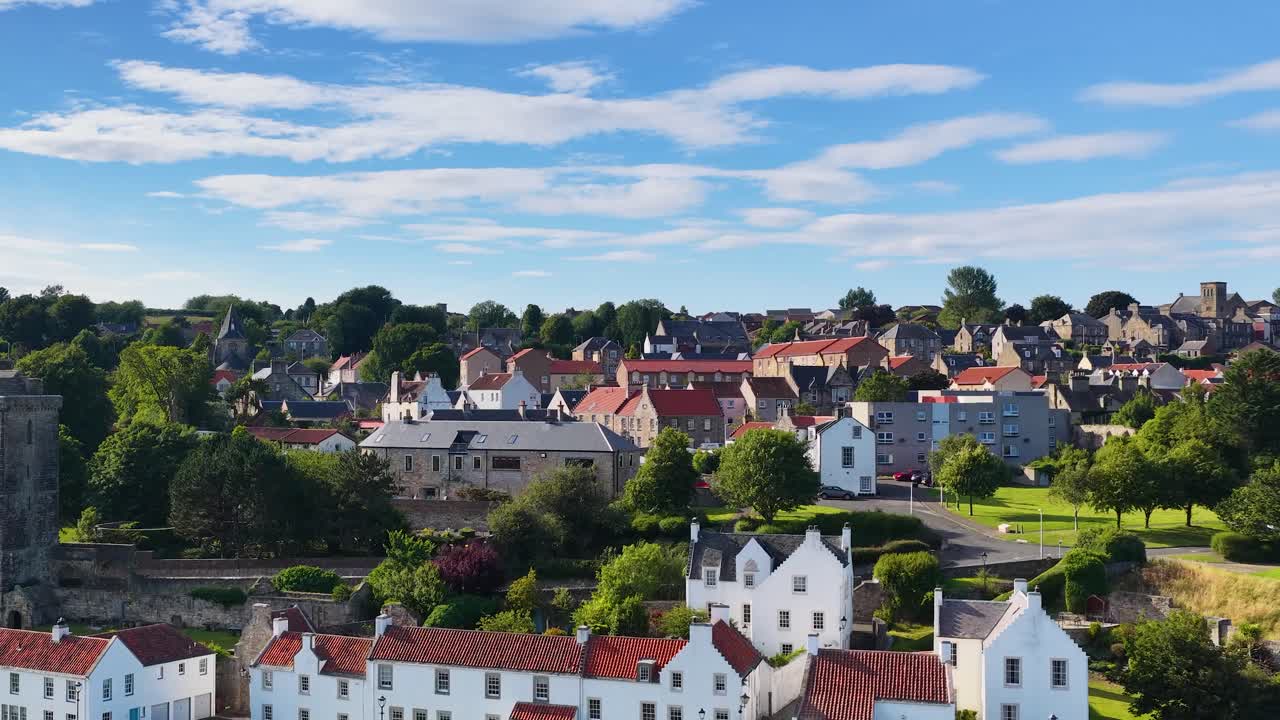 Daytime lateral pan across Fife village, white houses, red roofs, stone tower, and lush greenery