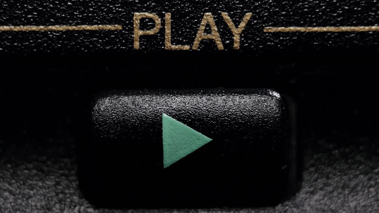 Close-up view of a black play button with a teal arrow being pressed on a vintage device