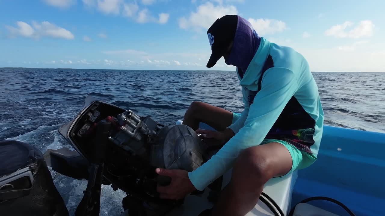 A young man opens the engine of a fishing boat while at sea to repair it.