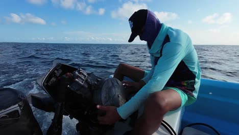 a young man opens the engine of a fishing boat while at sea to repair it.