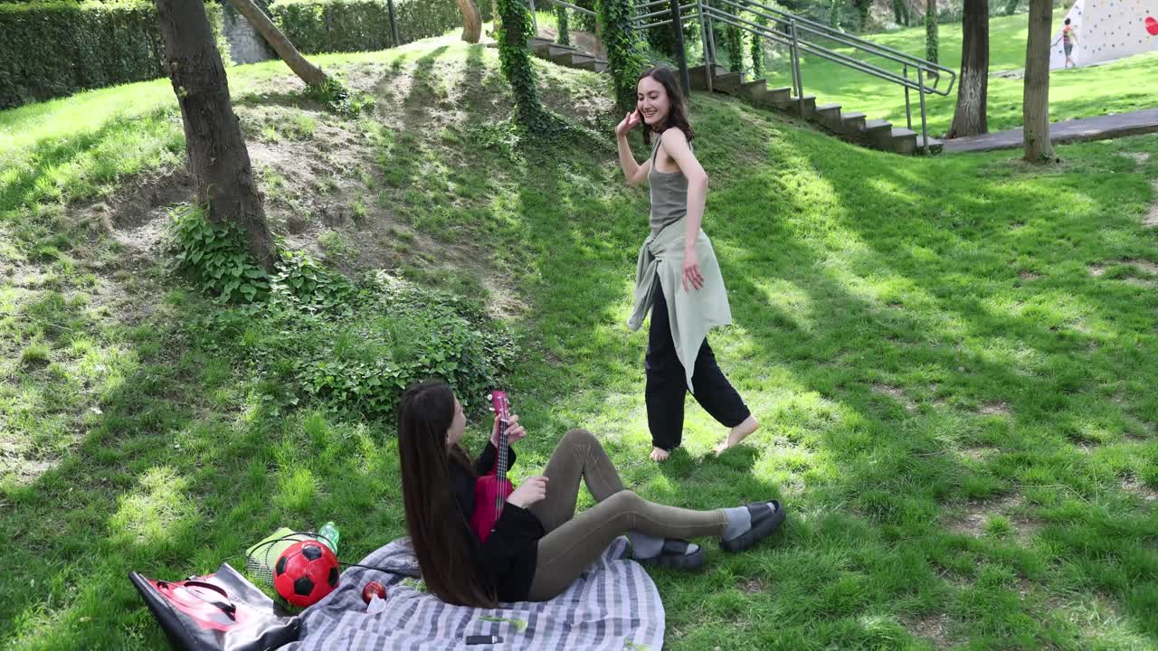 Donna balla mentre la fidanzata suona l'ukulele durante un picnic al parco