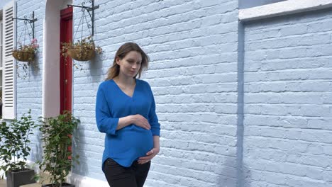 attractive pregnant caucasian woman carrying her belly down a street