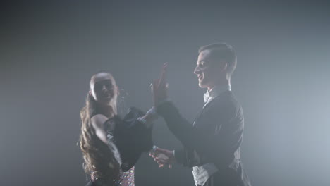 gorgeous ballroom dancers posing camera on dark stage. couple dancing indoors.