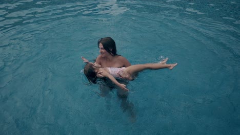 mujer sostiene en las manos y giros linda niña en el agua