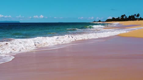 hd hawaii kauai slow motion low trucking shot with beach along bottom toward frame right with ocean waves crashing and washing across frame from left to right with an island in distance frame left