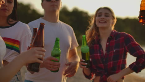 group of young people celebrate the end of the semester with beer. they clink and drink beer on the open air party.