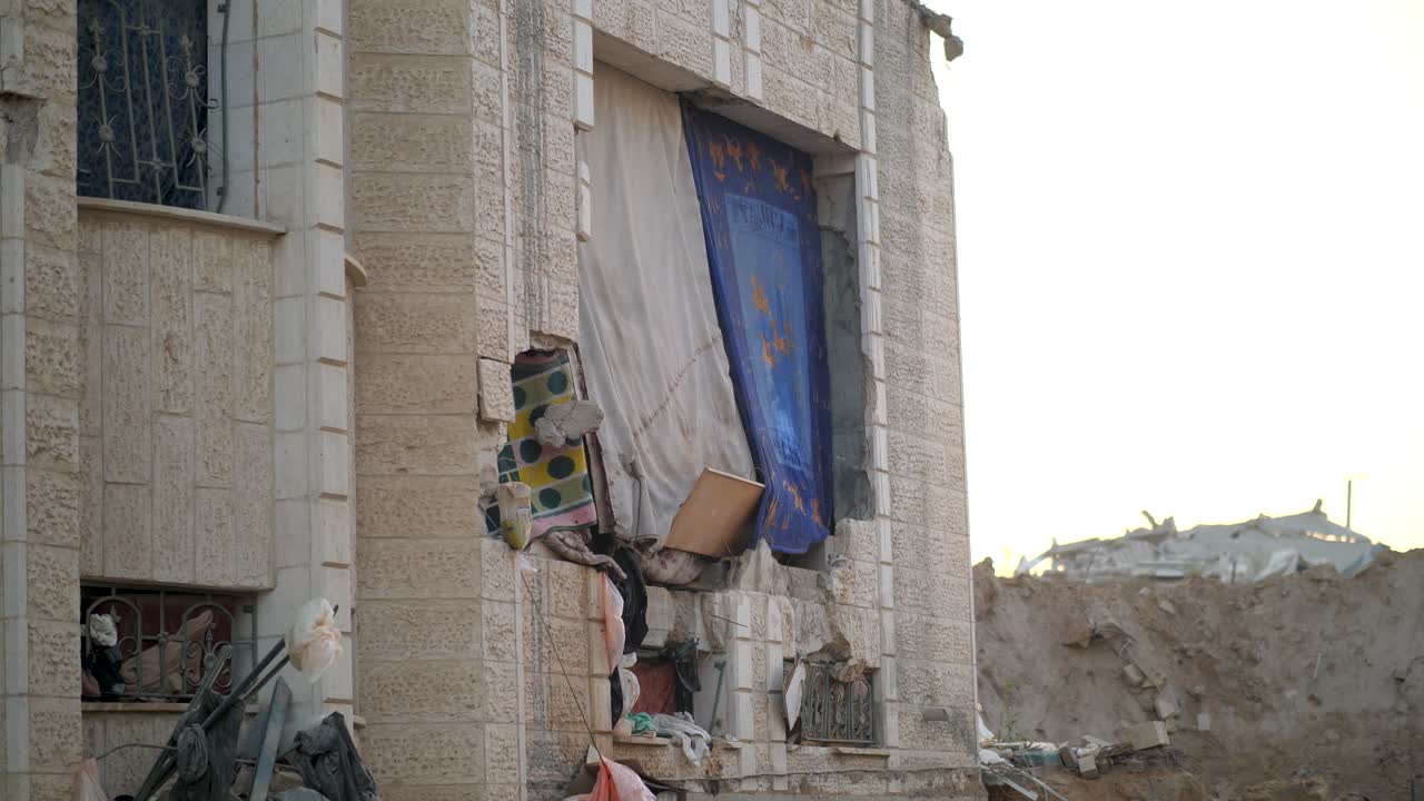 Facade of a bombed building in Gaza, where curtains, blankets, and fabric pieces are used to cover gaping holes and damage after destruction. Palestine