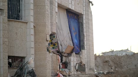 facade of a bombed building in gaza, where curtains, blankets, and fabric pieces are used to cover gaping holes and damage after destruction. palestine
