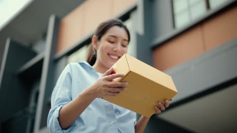 close up parcel in hand of blue uniform delivery man to customer front of the house with good service from shopping online. courier man delivering a cardboard box postal package to destination.