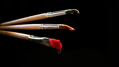 three wet brushes from which drops of paint drip