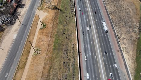 From-a-highway-teeming-with-commercial-vehicles,-this-drone-shot-pans-up-to-disclose-a-power-station-and-city-skyline,-framed-by-a-small-valley