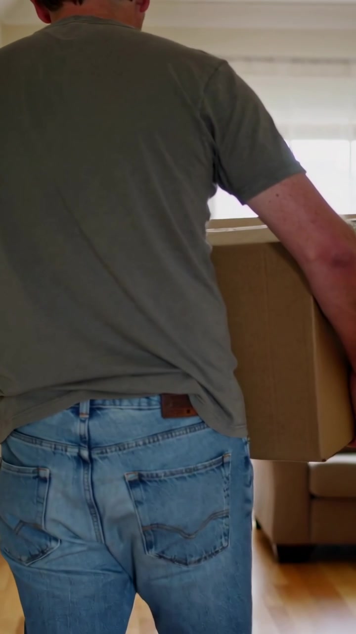 Vertical video: Carrying man grey tee jeans walking from hall into living room bringing box to sofa