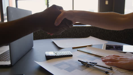 Close-up-of-young-mixed-race-business-team-shaking-hands-and-sitting-at-desk-of-modern-office-4k