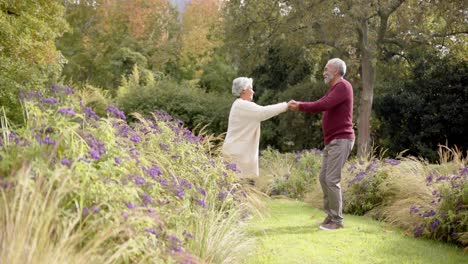 Senior-biracial-couple-dancing-together-in-sunny-garden,-unaltered,-copy-space,-in-slow-motion