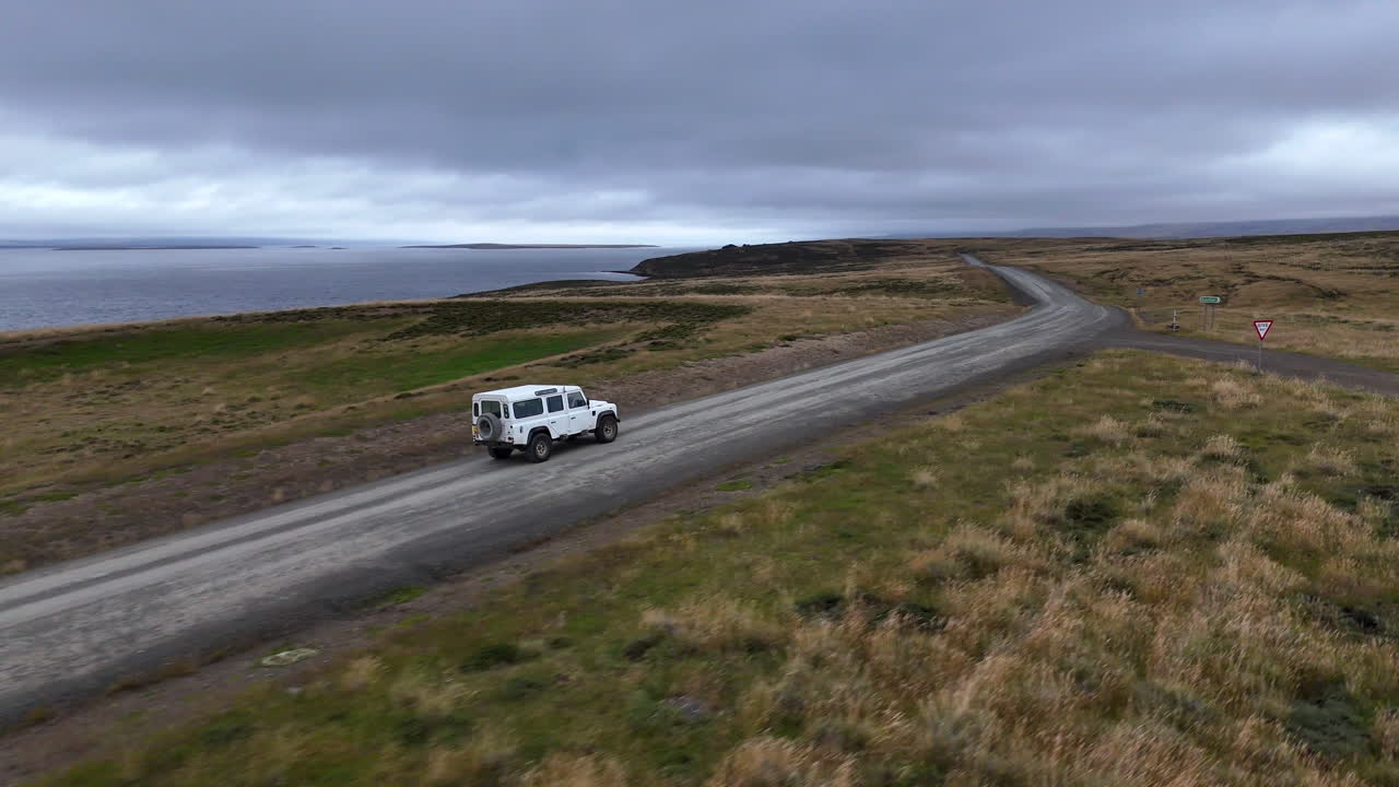 Filmato cinematografico con drone di un'auto che guida attraverso un paesaggio costiero remoto nelle Isole Falkland, riprese aeree