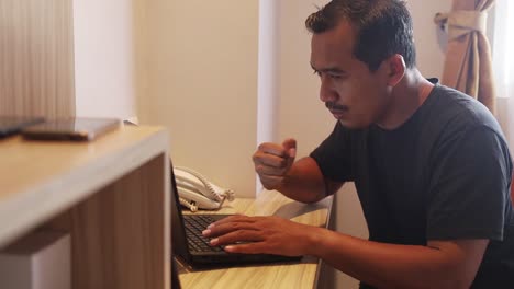 portrait of happy excited asian man working using laptop in hotel room