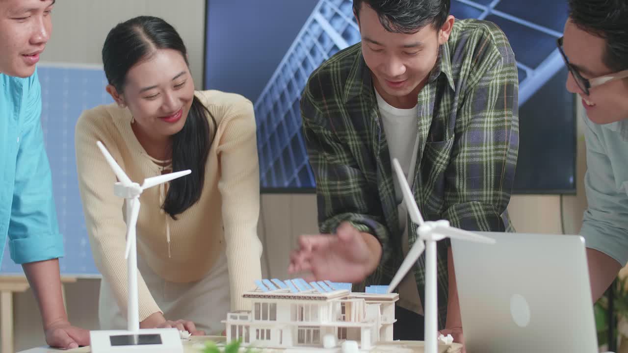 아시아 엔지니어 그룹이 사무실에서 태양 전지판을 가진 작은 집의 모델을 조립하는 것을 축하하는 클로즈업