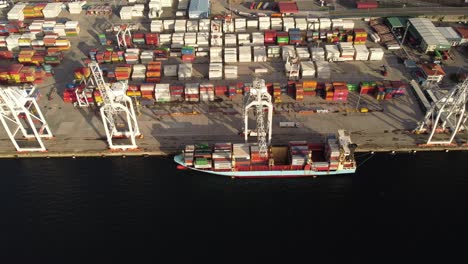 Vista-Aérea-De-Un-Barco-De-Carga-De-Contenedores-De-Envío-Con-Grúa-Trabajando-Importación-Exportación-Cadena-Alimentaria-Capitalismo-Consumismo-Concepto