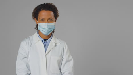 studio portrait of smiling female doctor or lab worker wearing face mask in white coat