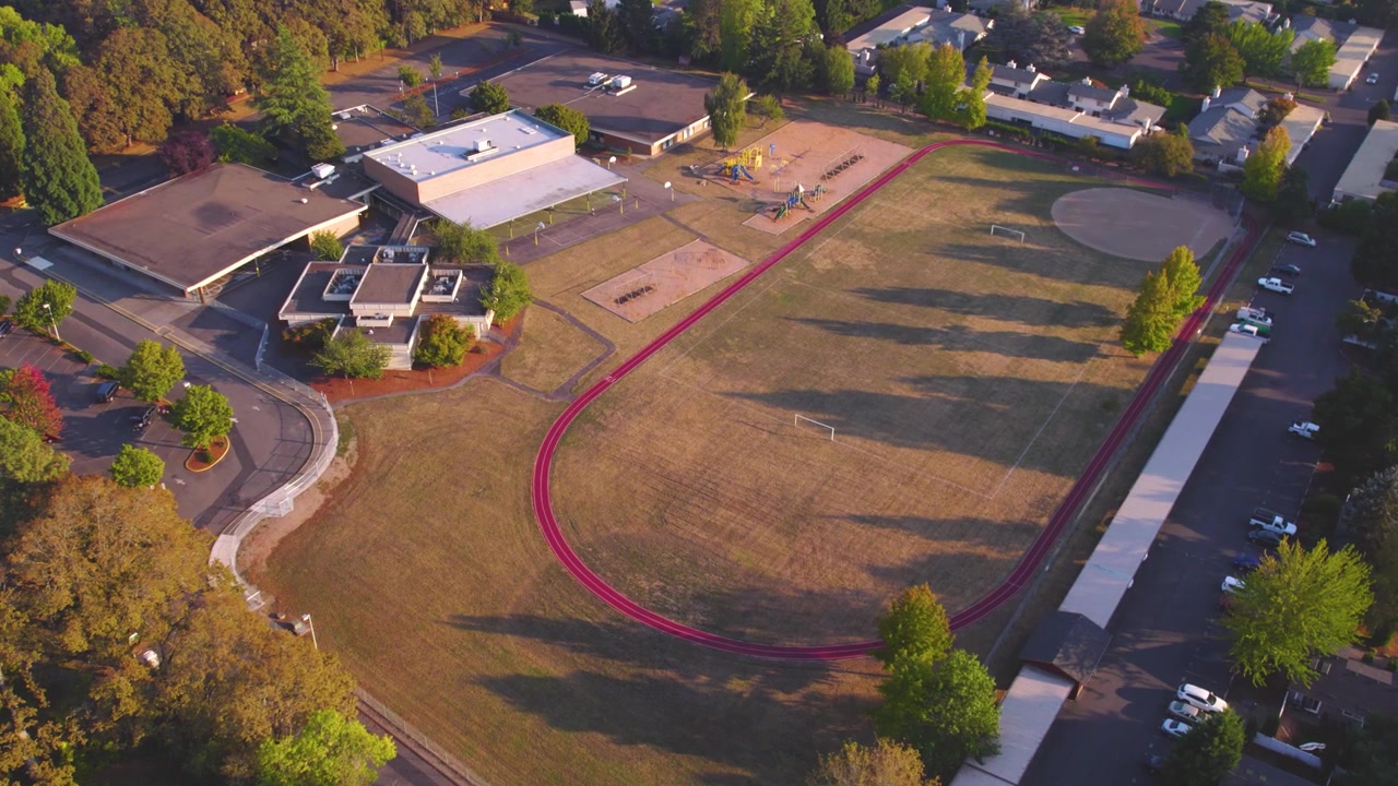 Luftaufnahme, die über einem Schulhof und einem weitläufigen Baseballfeld mit einer umlaufenden Laufbahn im Hintergrund absteigt