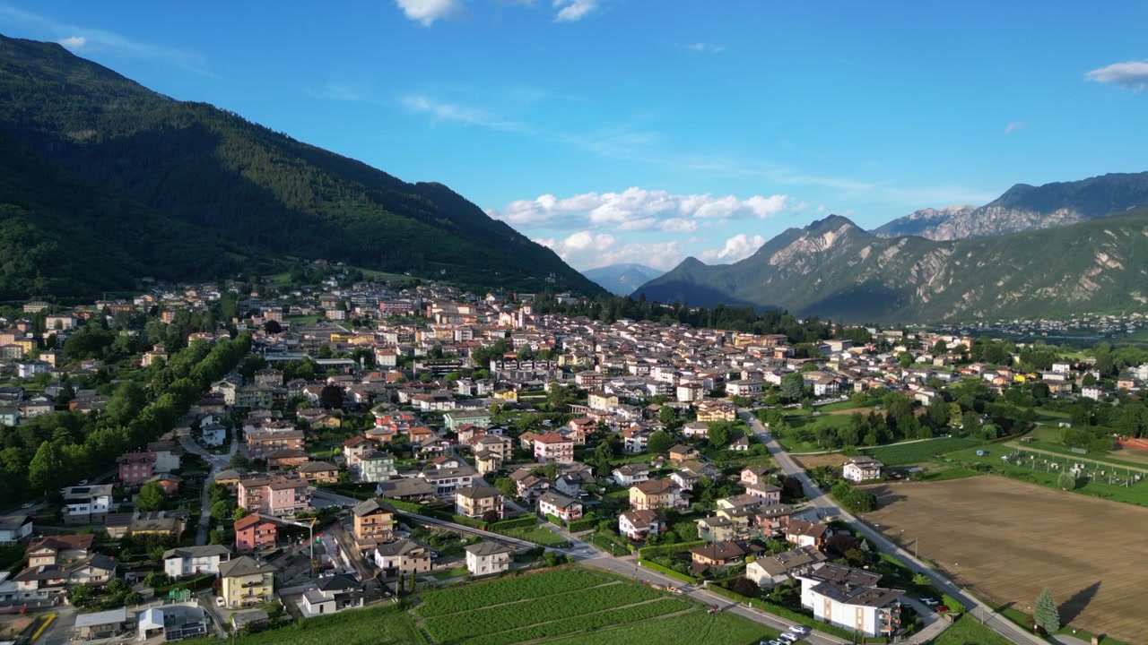 Ripresa con drone del villaggio di Levico Terme in Trentino con ampi campi verdi e sfondo montuoso nell'Italia settentrionale.