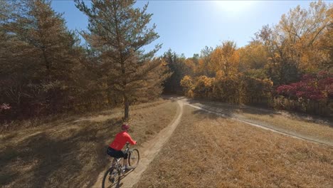 fpv drone following mountain biker biking on a dirt path during autumn season