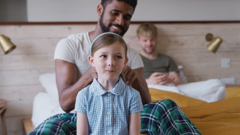 same sex male couple at home getting daughter ready for school plaiting her hair