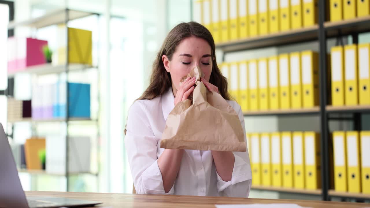Woman breathing into paper bag due to panic or anxiety in office