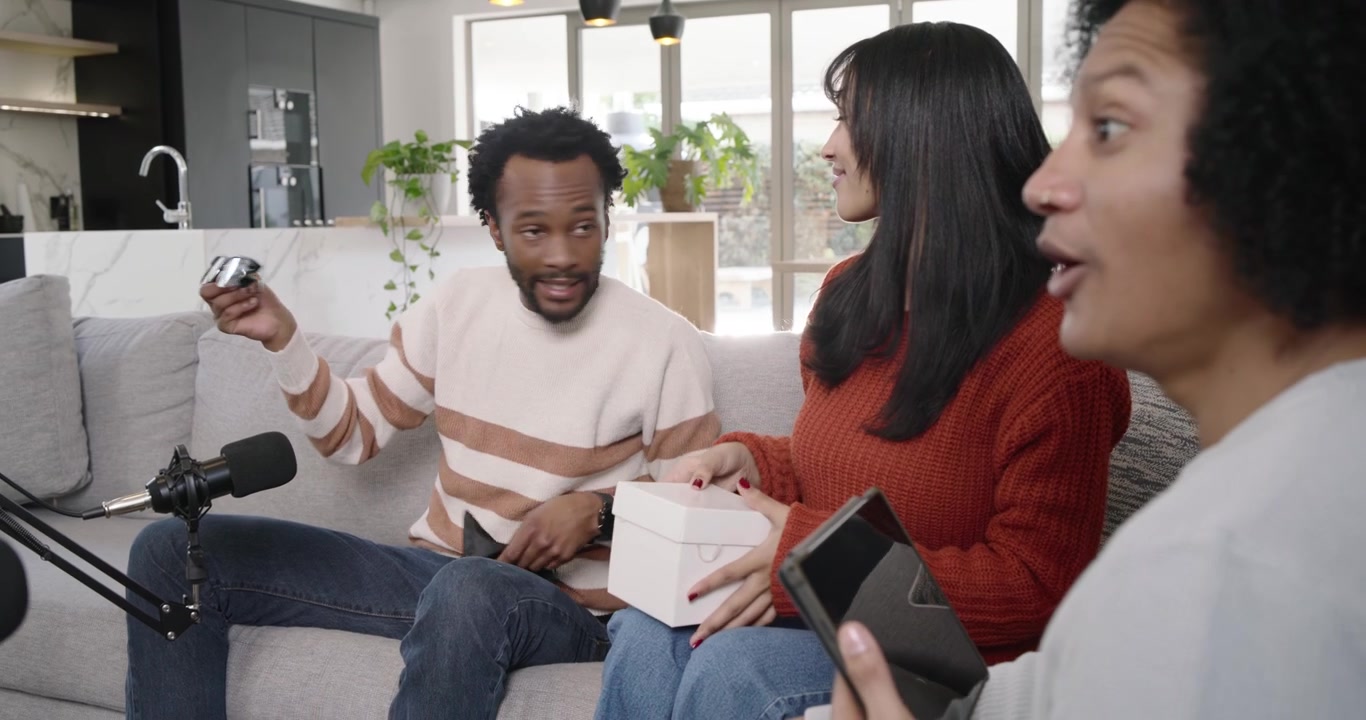 Forskellige værter filmer en demo med mikrofoner på sofaen, mens en afroamerikansk mand åbner en hvid kasse